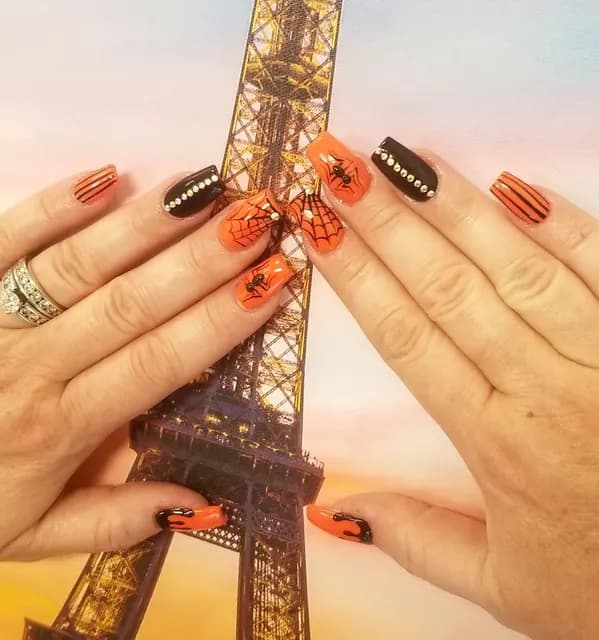Clientβs orange and black Halloween nail art held up in front of an Eiffel Tower picture
