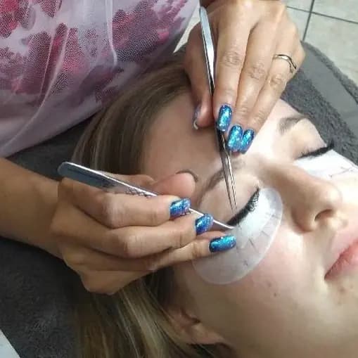 Lash artist with jeweled nails placing an extension on a client wearing eye pads